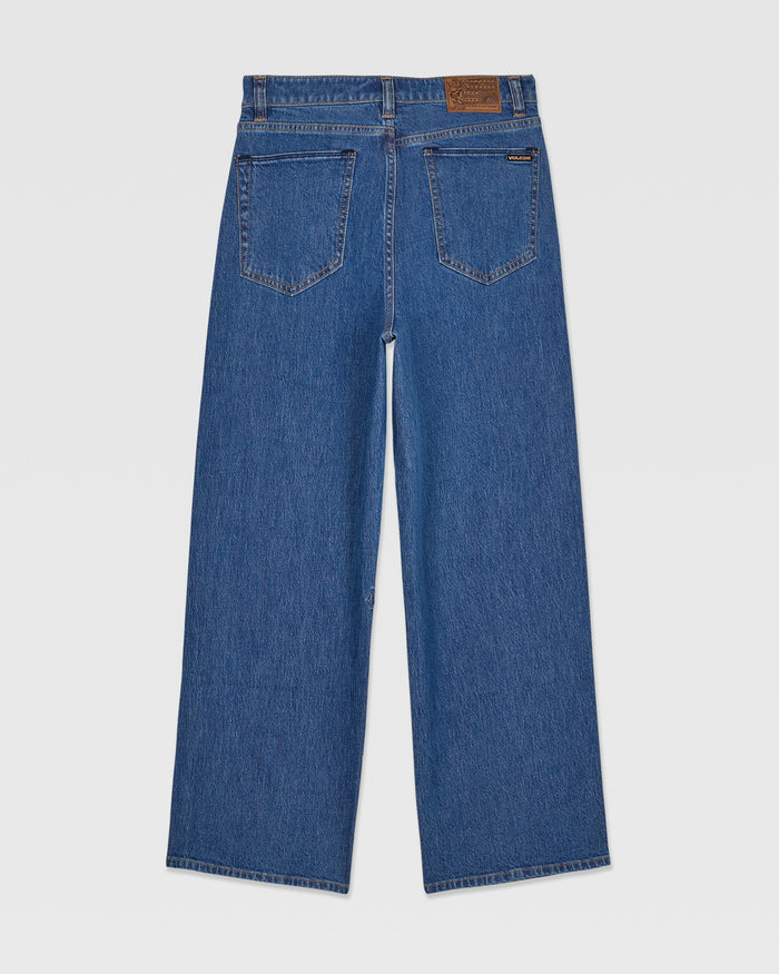 The Kids' Billow Denim II Pants by Volcom are medium wash, wide-leg jeans with a loose low-rise fit. Shown from the back, they feature two back pockets, visible stitching, and a brown leather patch on the waistband.