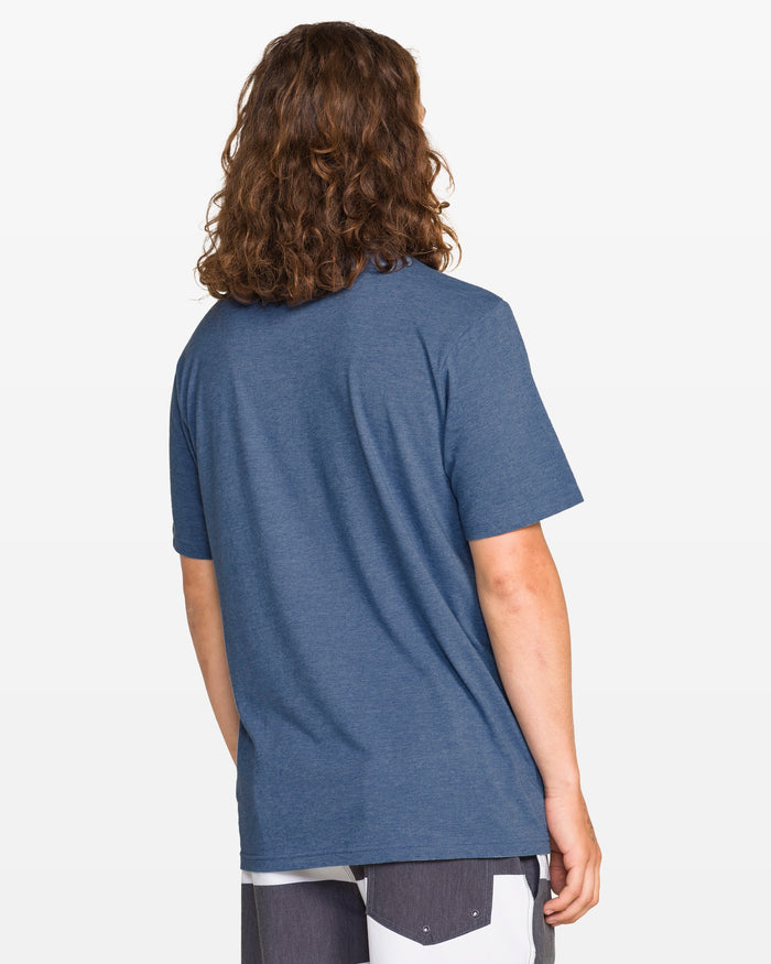 A person with long, wavy brown hair faces away, wearing Volcom Men's Men modern fit t-shirt and color-block shorts against a plain white background.