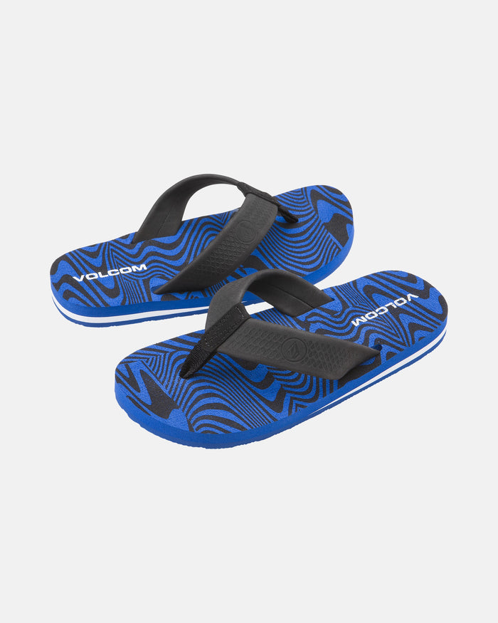 The Kids' Daycation 2 Big Youth sandals by Volcom feature a blue and black wavy abstract pattern, VOLCOM branding on the footbeds, and Recliner Comfort Foam for arch support, shown on a white background.