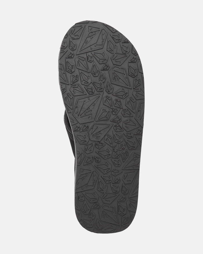 The image shows the underside of a black Volcom Kids' Recliner 2 Big Youth sandal with a textured rubber sole featuring geometric shapes and angular patterns, designed for arch support.