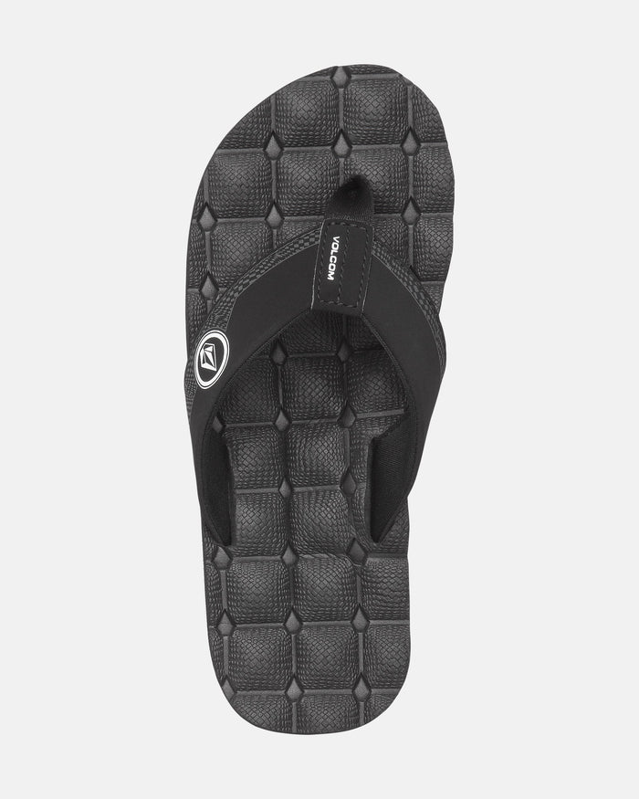 The Volcom Kids' Recliner 2 Big Youth sandal features a black fabric thong strap with a small circular logo and VOLCOM tag, plus a geometric-textured comfort foam footbed. Shown against a light gray background.