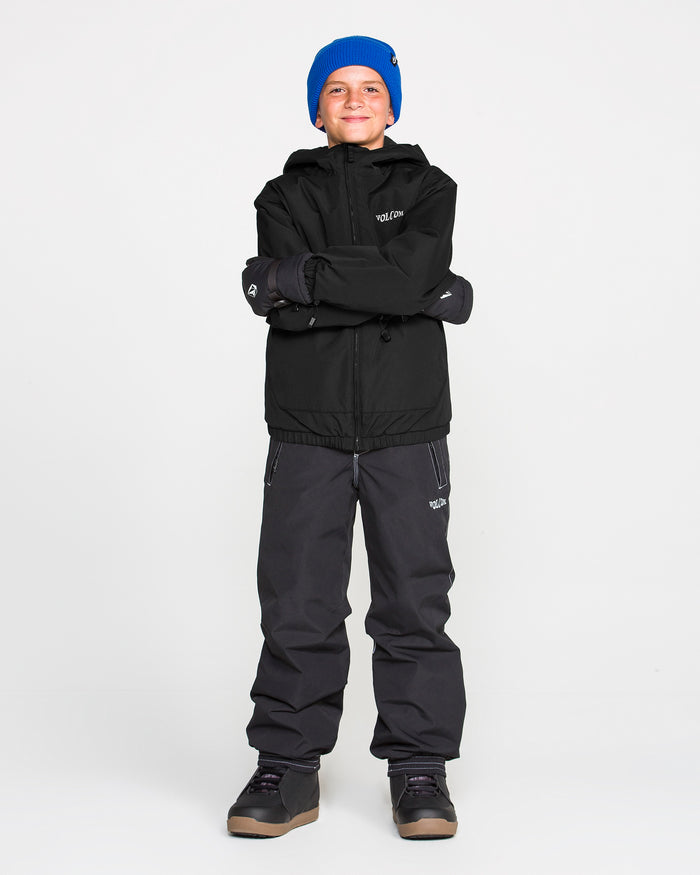 A smiling child wearing a blue beanie, dark pants, and the Volcom Kids’ Youth Chaos Insulated Jacket in black—featuring weather defense and recycled insulation—stands with arms crossed against a plain white background.