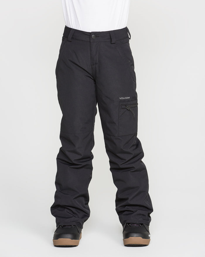 A person is wearing black Volcom Kids’ Frostique Insulated Pants with recycled insulation and black boots, standing against a plain white background. These pants feature an adjustable waist, a zippered pocket on the right thigh, and belt loops at the waist.