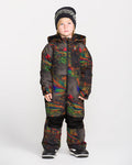 A young child wearing the Volcom Kids’ Kid’s Little Flurry One Piece—crafted with recycled V-Science fabric and warm insulation in a colorful, patterned design—is styled with black winter boots and a black beanie, standing against a plain white background and looking slightly to the side.