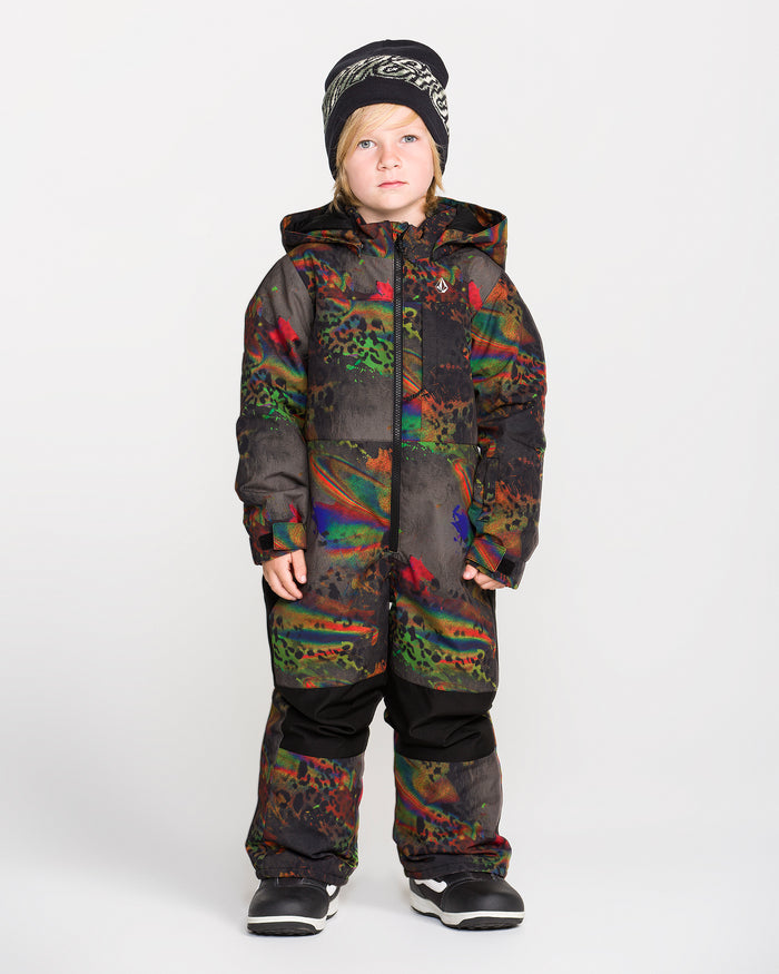 A young child wearing the Volcom Kids’ Kid’s Little Flurry One Piece—crafted with recycled V-Science fabric and warm insulation in a colorful, patterned design—is styled with black winter boots and a black beanie, standing against a plain white background and looking slightly to the side.