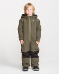 A young child with blonde hair stands against a plain white background, dressed in the Volcom Kids’ Little Flurry One Piece snowboard suit in olive green, which features black knee patches and black boots. This insulated snowsuit is crafted from recycled V-Science materials for warmth and sustainability.