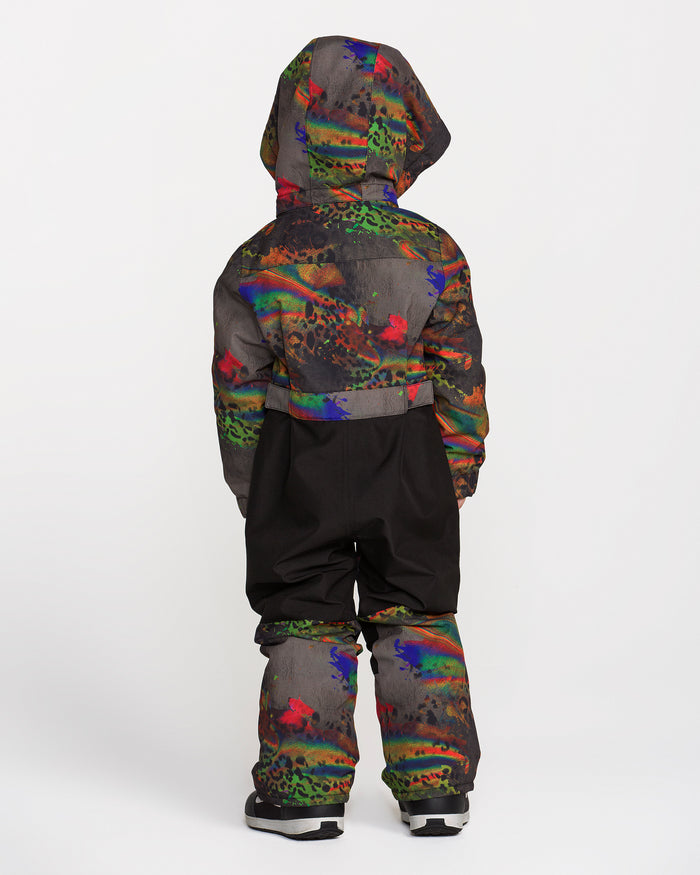 A child is seen from behind wearing the Volcom Kids’ Little Flurry One Piece—a hooded snowsuit adorned with colorful patterns, designed with cozy insulation and a helmet-compatible removable hood—set against a plain white background.