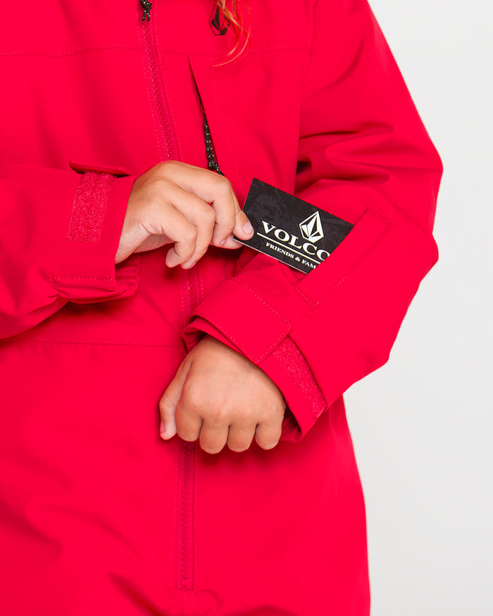 A child wearing the Volcom Kids’ Little Flurry One Piece, featuring recycled V-Science fabric, slips a black Volcom-branded card into the small zippered pocket on the sleeve.