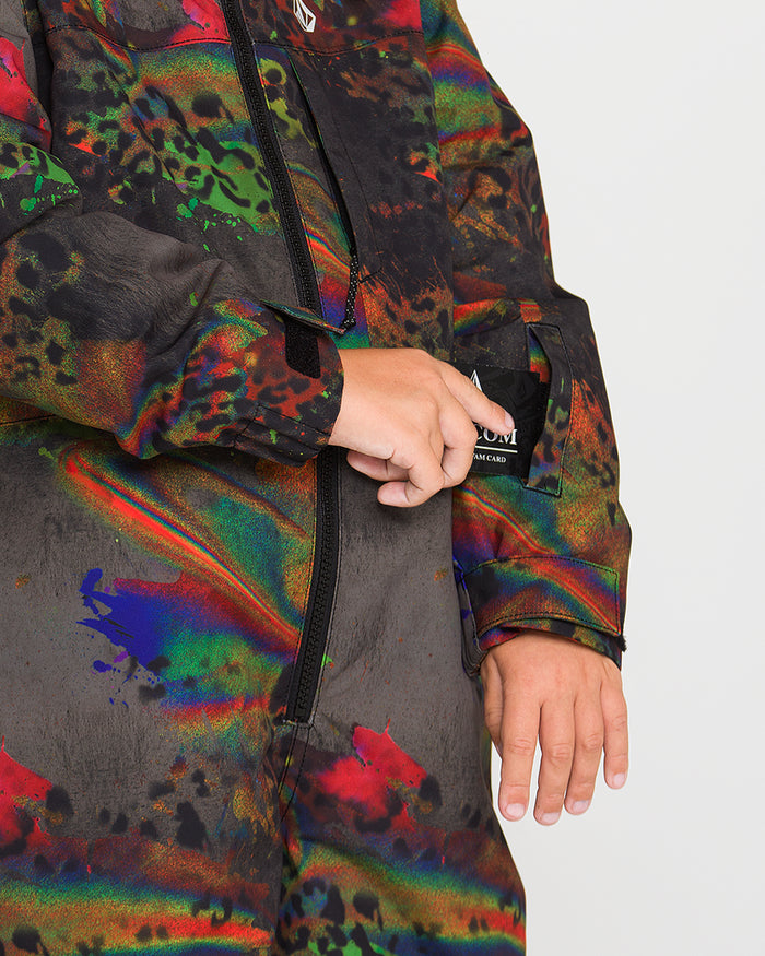 A child wearing the Volcom Kids’ Little Flurry One Piece—a colorful, abstract-patterned outerwear zippered at the front, made from recycled V-Science fabric with warm insulation—is placing a card into a small pocket on the sleeve. Only the torso and hands are visible.