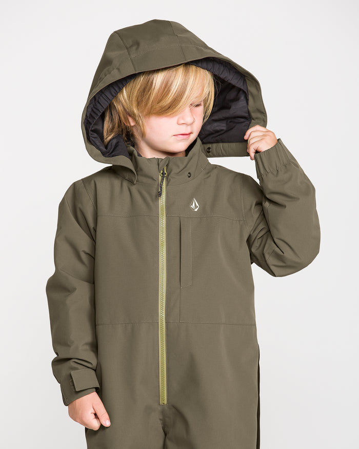 A young child with blonde hair wears the Volcom Kids’ Little Flurry One Piece, an olive green hooded jumpsuit made from recycled V-Science fabric, looking down and holding the side of the hood against a plain white background.