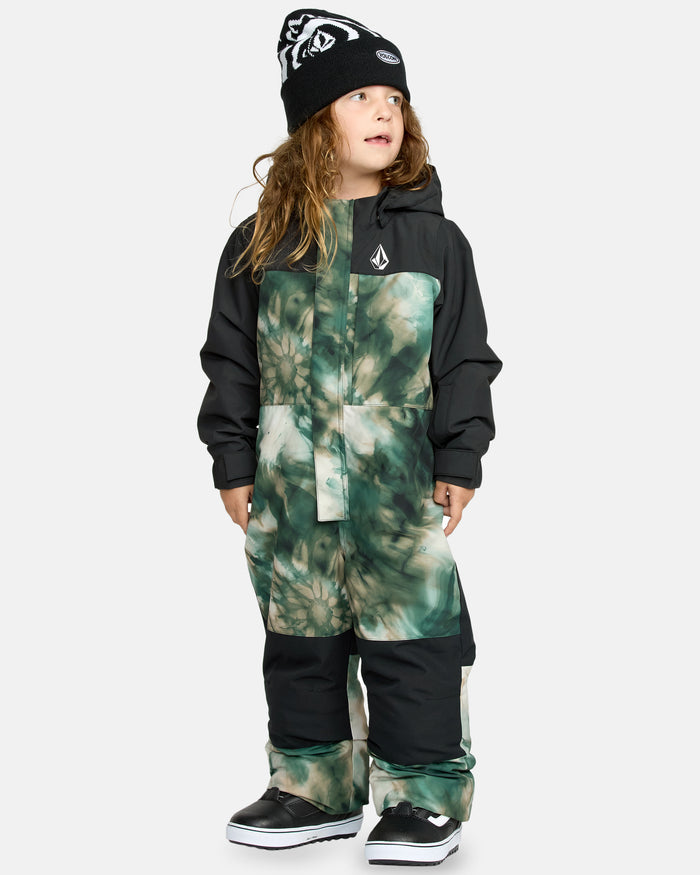 A young child wearing the Kids' Little Flurry One Piece, black winter boots, and a black beanie with white patterns stands against a plain light background, looking off to the side.