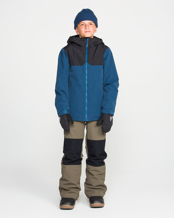A young person wearing a blue beanie, a blue and black winter jacket with waterproof insulation, Volcom Kids’ Youth Barkley Insulated Bib snow pants in olive and black featuring Grow-Tech youth bibs, black gloves, and black boots stands against a plain white background.