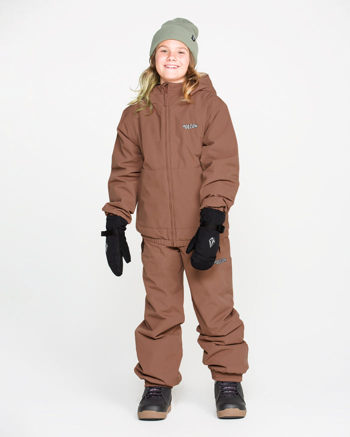 A smiling child wearing a brown winter jacket and Volcom Kids’ Youth Chaos Insulated Pants, which feature V-Science 2-Layer fabric and recycled insulation, paired with black gloves, gray boots, and a light green beanie, stands against a plain white background.