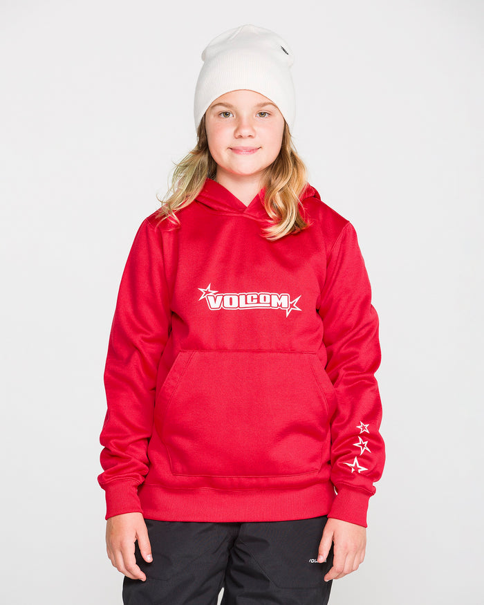 A young person wearing a Volcom Kids’ Youth Hydro Fleece Hoodie in red, featuring hydrophobic fleece, star details on the sleeve, and a cozy handwarmer pocket, along with a white beanie and black pants, stands against a plain white background smiling softly.