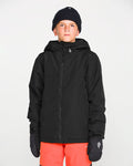 A young person wearing a black beanie, black gloves, bright orange pants, and the Volcom Kids’ Youth Stone.91 Insulated Jacket with Grow-Tech features stands facing forward against a plain white background.