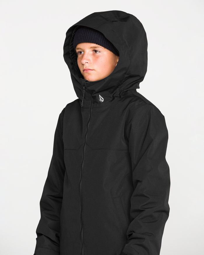 A young person wearing the Volcom Kids’ Youth Stone.91 Insulated Jacket in black, featuring innovative Grow-Tech technology and recycled insulation, along with a black beanie, looks forward with a neutral expression against a plain light background.