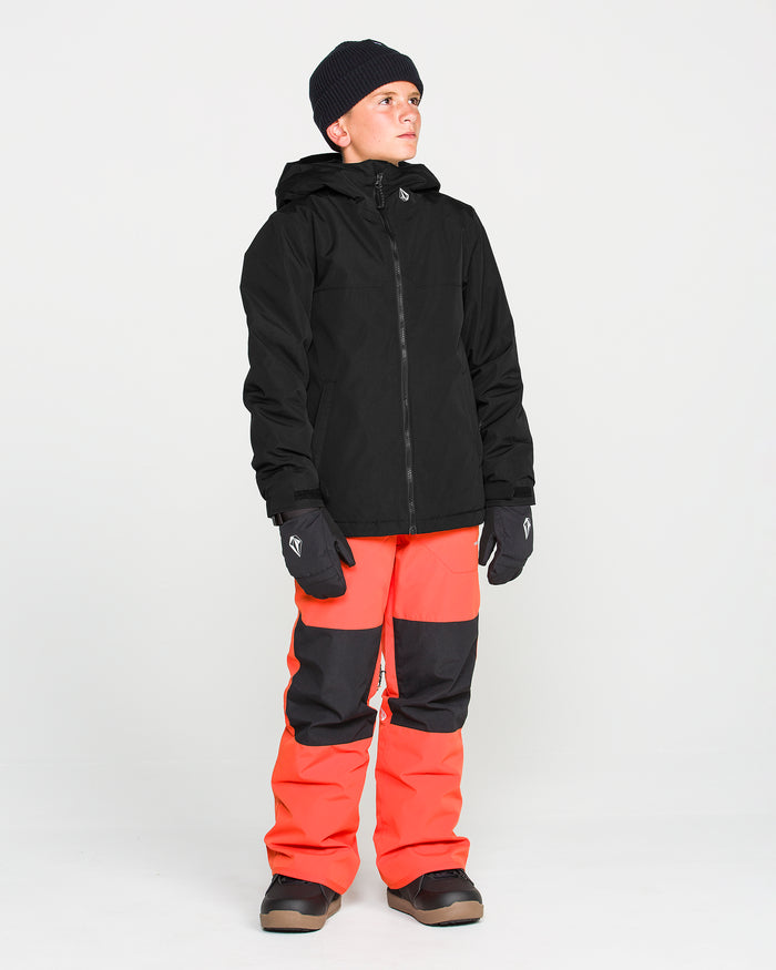 A young person wearing the Volcom Kids’ Youth Stone.91 Insulated Jacket, featuring recycled insulation, along with black gloves, a dark knit beanie, and bright orange snow pants with black patches, stands facing slightly to the side against a plain white background.