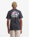 A man with short blond hair wears the Volcom Men's Allegiance Short Sleeve Tee, featuring "VOLCOM HAWAII" text, a Hawaii outline, and flag graphic on the back, standing against a plain white background.