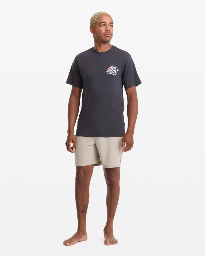 A person with short blonde hair wears the Volcom Men's Allegiance Short Sleeve Tee, featuring a small left chest graphic, and light beige shorts, standing barefoot against a plain white background.