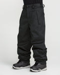 A person wearing Volcom Men’s Arthur 20K Pants in loose-fitting black recycled twill and black snowboard boots, standing against a plain white background.