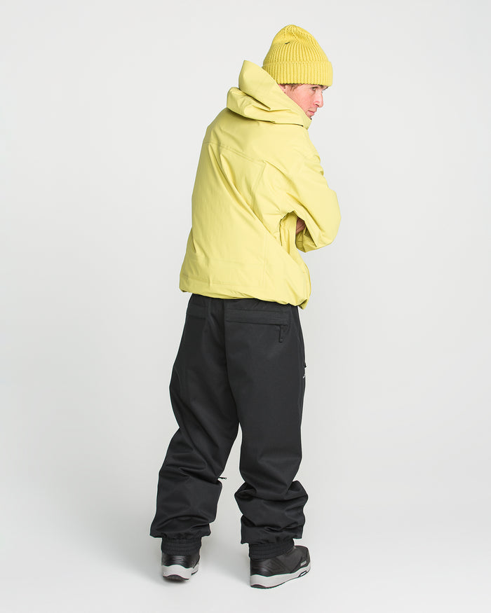 A person in a yellow jacket, yellow beanie, and black Volcom Men’s Arthur 20K Pants stands facing backward, looking over their shoulder against a plain white background.