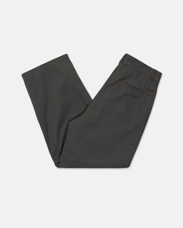 A pair of Men's Baggos Pleat Pants by Volcom in dark gray cotton, neatly folded in half with the waistband and back pocket visible against a white background.