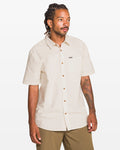 A man with dreadlocks and a tattoo on his left arm wears the Volcom Men's Bankstone II Short Sleeve Tee and khaki pants, standing against a plain white background.