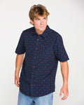 A person with light brown hair wears the Volcom Men's Bankstone Short Sleeve Shirt in a classic fit, featuring a subtle dobby weave pattern in navy, paired with light blue jeans and standing against a plain white background.