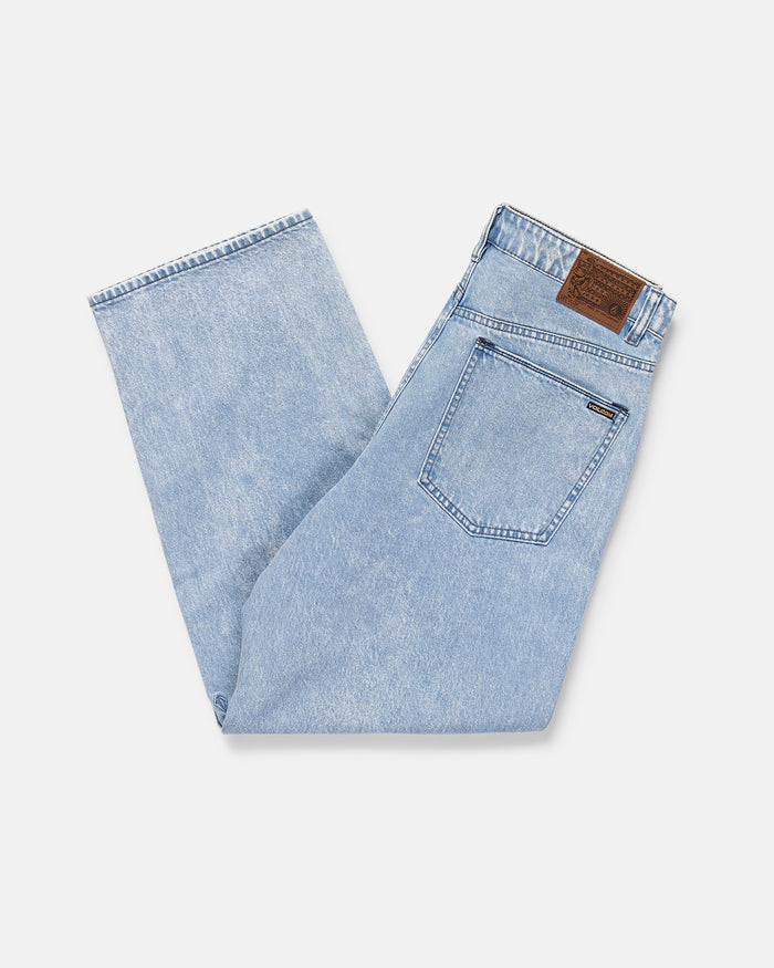A pair of light blue Volcom Men's Billow Denim Pant, neatly folded on a white background, with a brown leather waistband patch, visible contrast-stitched back pocket, and made from recycled cotton for sustainability.