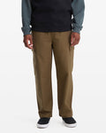 A man in Volcom Men's Billow Tapered Cargo Pants with an elastic waist, a dark long-sleeve shirt with lighter sleeves, and black slip-on shoes stands facing forward against a plain white background.
