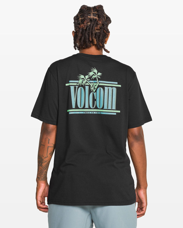 A person with braided hair, seen from behind, wears a Volcom Men's Breathe Deep Short Sleeve Tee in black with a turquoise palm tree logo, plus light gray shorts and a left arm tattoo.