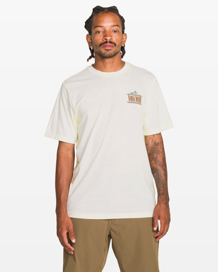 A person with dreadlocks and tattoos on their right arm wears the Volcom Men's Breathe Deep Short Sleeve Tee in heather, featuring a small left chest graphic, paired with khaki shorts, standing against a plain white background.
