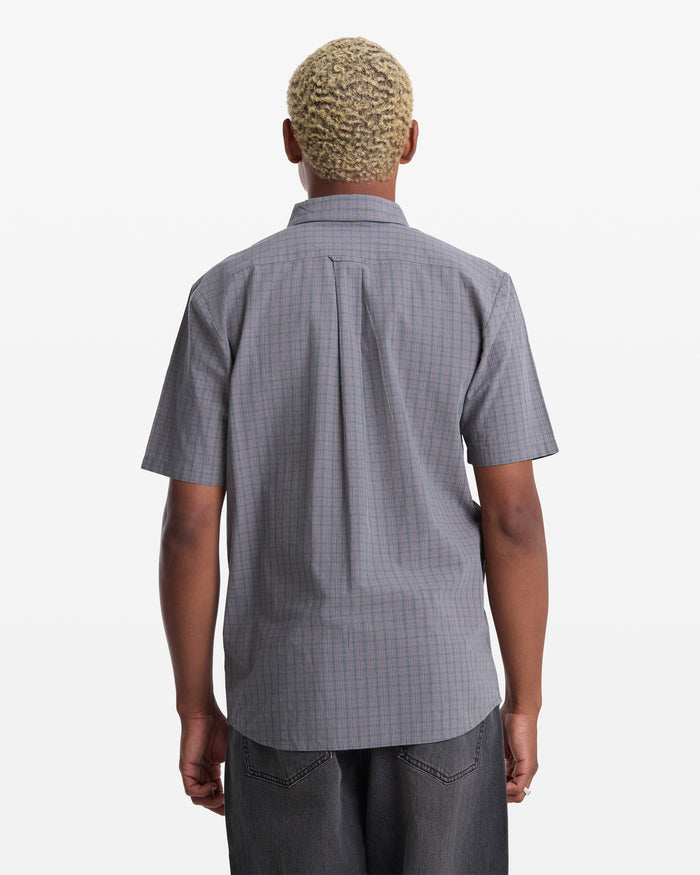 A person with short, light-blond curly hair is seen from behind, wearing the Volcom Men's Brewster Short Sleeve shirt and dark pants against a plain white background.