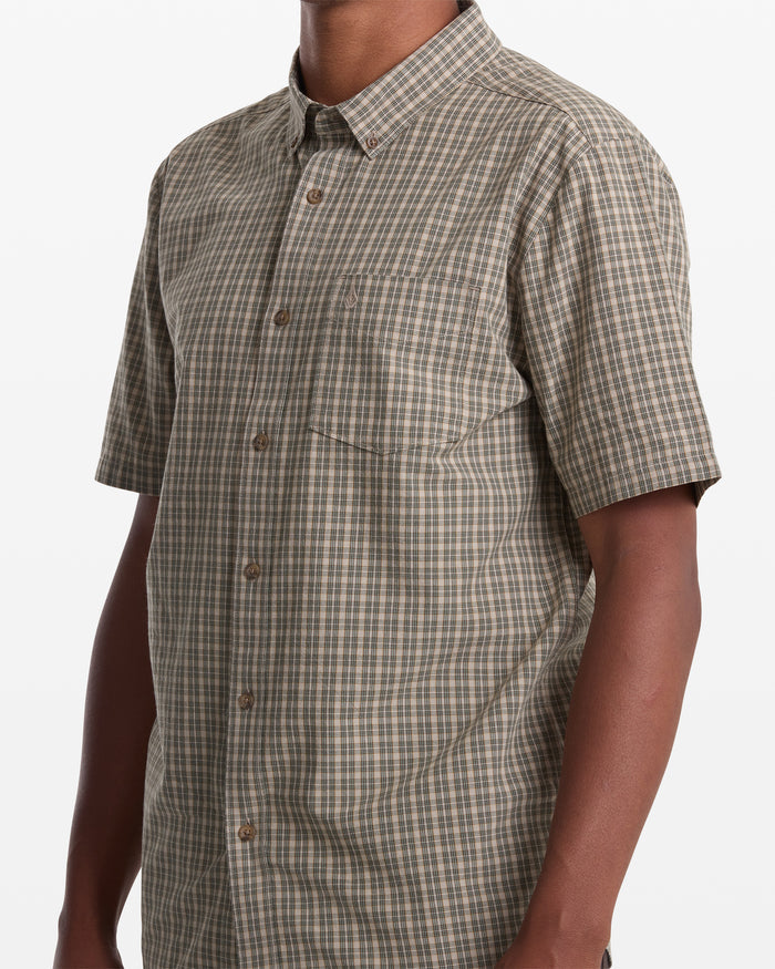 A man wears the Volcom Men's Brewster Short Sleeve, a brown and green checkered button-up, shown from shoulders to waist against a white background.