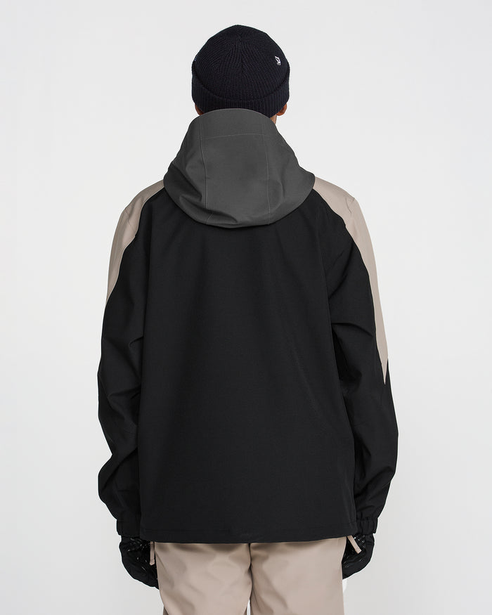 A person facing away, wearing the Volcom Men’s Brighton Full Zip Jacket in black and taupe—featuring V-Science 2-Layer construction and PFAS-free DWR—paired with beige pants, black gloves, and a dark knit beanie, against a plain white background.
