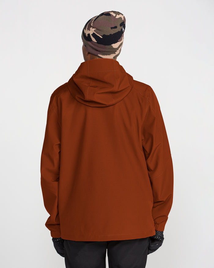 A person, seen from behind against a plain white background, wears the Volcom Men’s Brighton Full Zip Jacket in rust color featuring V-Science 2-Layer protection, black pants with a Zip Tech jacket-to-pant interface, gloves, and a camo beanie.