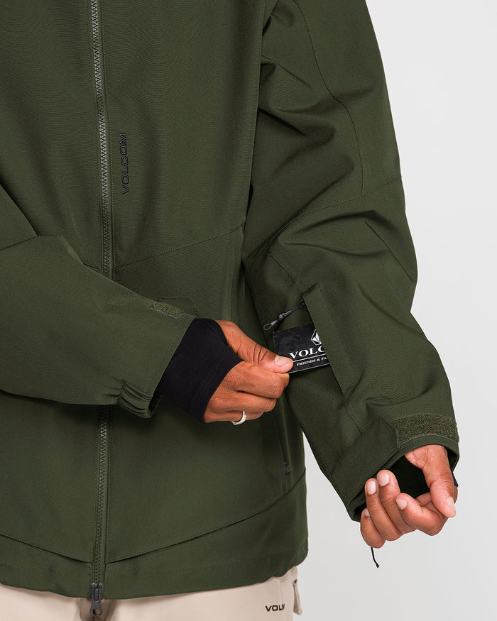 A person wearing the Volcom Men’s Brighton Full Zip Jacket in olive green opens a small zippered pocket on the sleeve, revealing a black VOLCOM label. Only the jacket, which features fully taped seams, and a partial hand are visible.