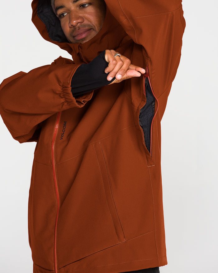 A person wearing the Volcom Men’s Brighton Full Zip Jacket in rust unzips an underarm vent, revealing the mesh lining inside. This V-Science 2-Layer jacket features red zippers, a PFAS-free DWR finish, and a relaxed fit.