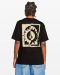 A person with short dreadlocks, seen from behind, wears the Volcom Men's Burner Short Sleeve Tee in black, featuring a large abstract beige graphic on the back, classic fit, paired with light blue jeans against a white background.