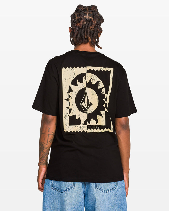 A person with short dreadlocks, seen from behind, wears the Volcom Men's Burner Short Sleeve Tee in black, featuring a large abstract beige graphic on the back, classic fit, paired with light blue jeans against a white background.