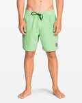 A barefoot person wears Volcom Men's Center Elastic Waist 17" Trunk swim shorts in light green, made from recycled polyester with 2-way stretch, featuring a black drawstring and small round logo on the left leg, against a plain white background.