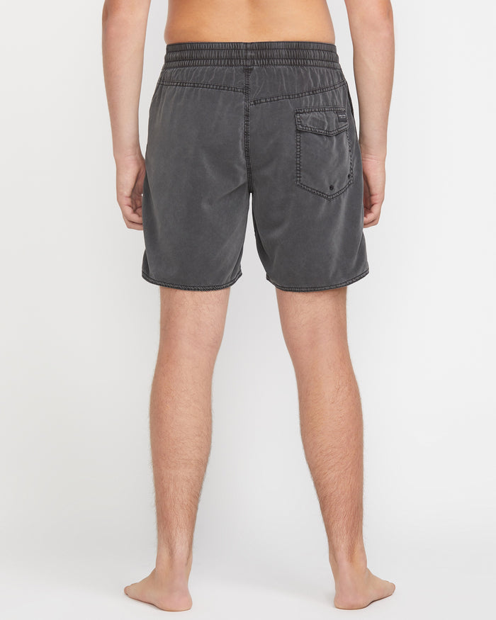 A person stands barefoot facing away, wearing Volcom Men's Center Elastic Waist 17" Trunk in charcoal gray with a single back pocket and mechanical stretch; the background is plain white.