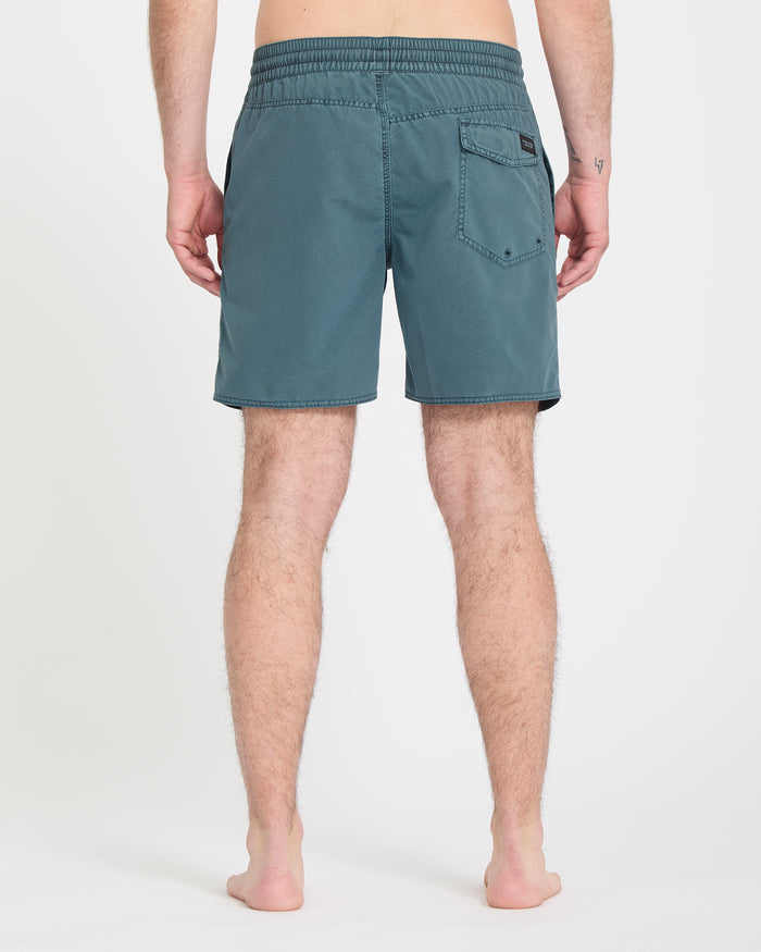 A person stands barefoot on a white background, shown from the back, wearing Volcom Men's Center Trunks 17 in teal with an elastic waistband and a single back pocket.