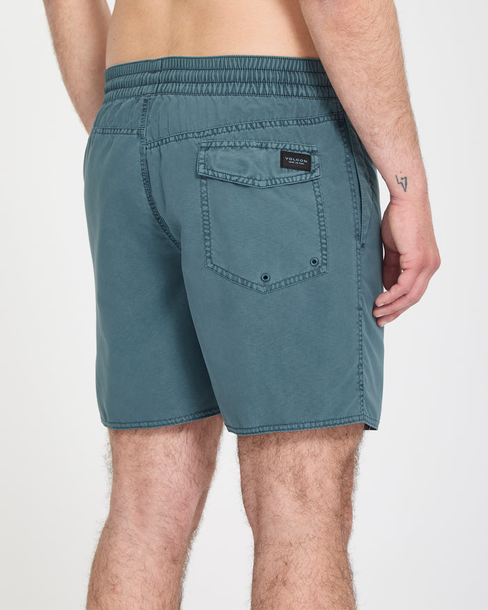 A person is seen from behind wearing Volcom Men's Center Trunks 17 in teal, featuring an elastic waistband and a back pocket, with their back, arm, and legs partially visible.