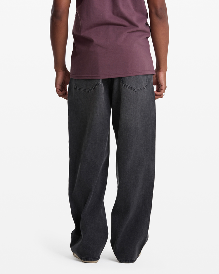 A person stands facing away from the camera, wearing Volcom's Men's Chillow Denim jeans with a maroon shirt, against a plain white background.