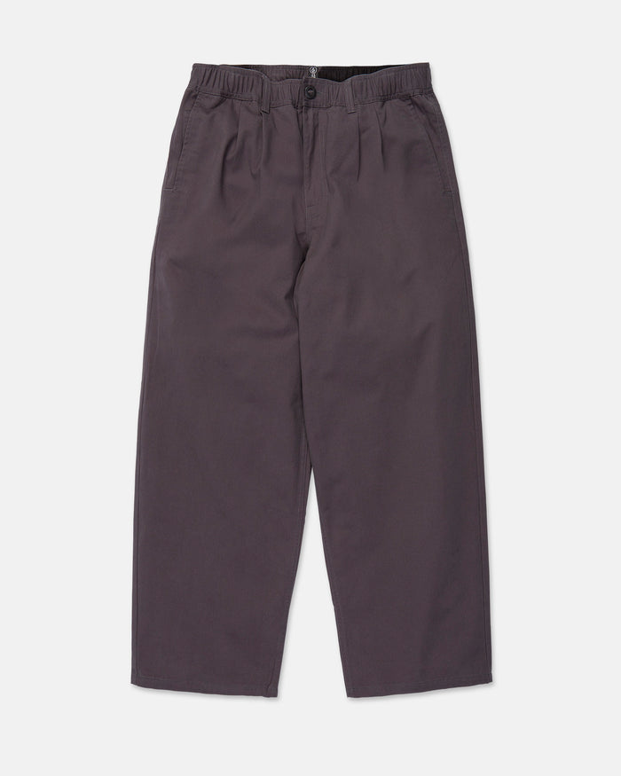 Volcom Men's Chillow Pleat Elastic Waist Pants in dark gray cotton twill, featuring a wide-leg silhouette, elastic waistband with button closure, and side pockets, laid flat on a white background.