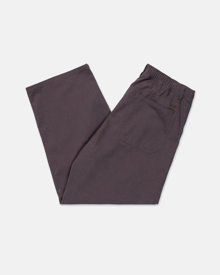 The Volcom Men's Chillow Pleat Elastic Waist Pants are made from dark gray cotton twill, with a relaxed, baggy fit and an elastic waistband. Shown here laid flat with one leg crossed over the other, these pants feature a back pocket on the right side.