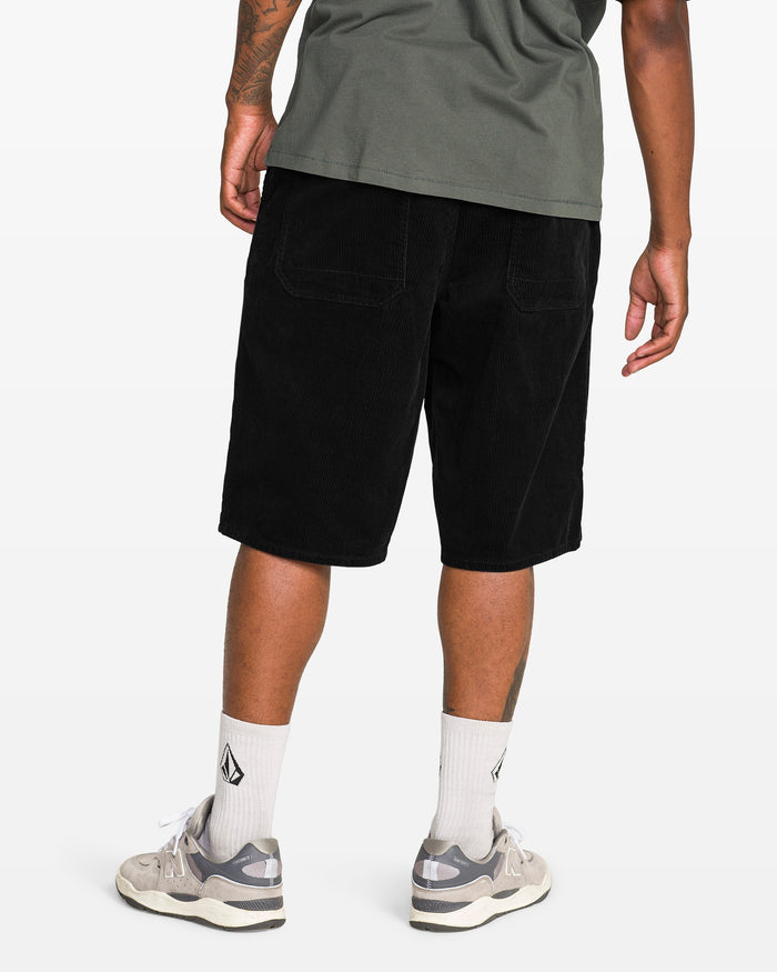 A person is seen from behind wearing a green t-shirt, white socks, gray sneakers, and Volcom Men's Chillow 24" Shorts in antique black, standing against a plain white background.
