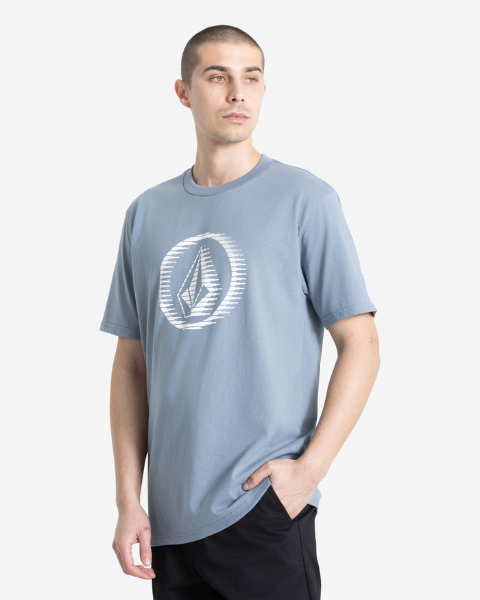 A man with short hair wears the Volcom Men's Circle Stone Short Sleeve Tee, made from 100% cotton and featuring a bold geometric logo. He stands with one hand in his pocket, looking to the side against a plain white background.
