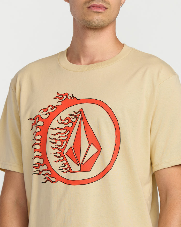 A person wears the Volcom Men's Circle Stone Short Sleeve Tee, a classic fit crew neck in premium ring spun cotton, featuring a large red geometric flame design inside a circle on the front. The head and crew neck are partially out of frame.